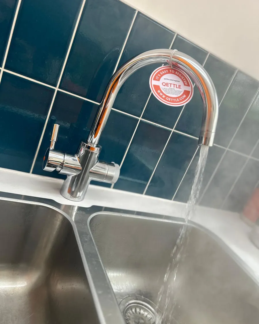 Chrome boiling water tap running into a stainless steel sink against teal tiles